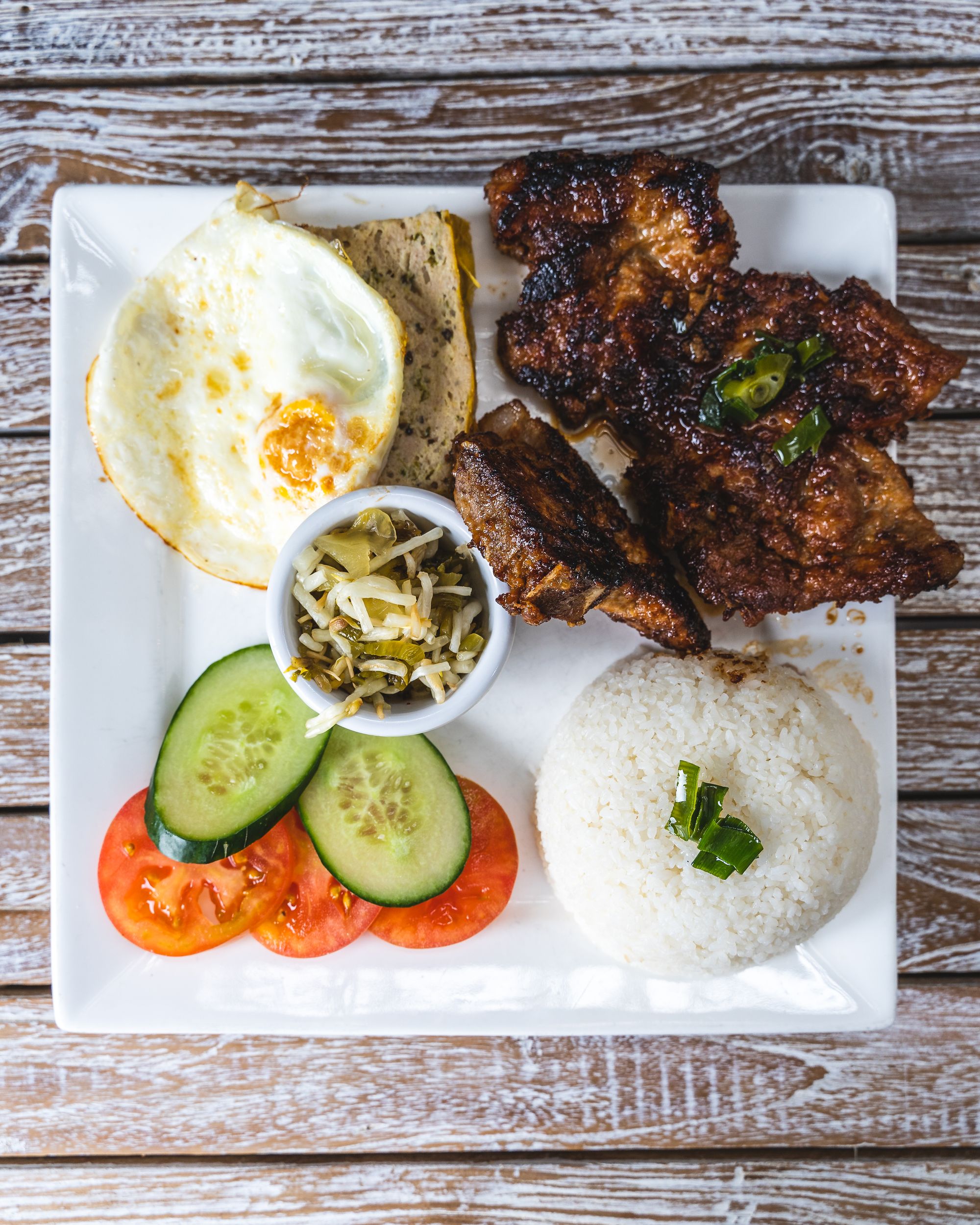 Overhead shot of broken rice with an egg, cucumber, tomato, grilled pork and rice