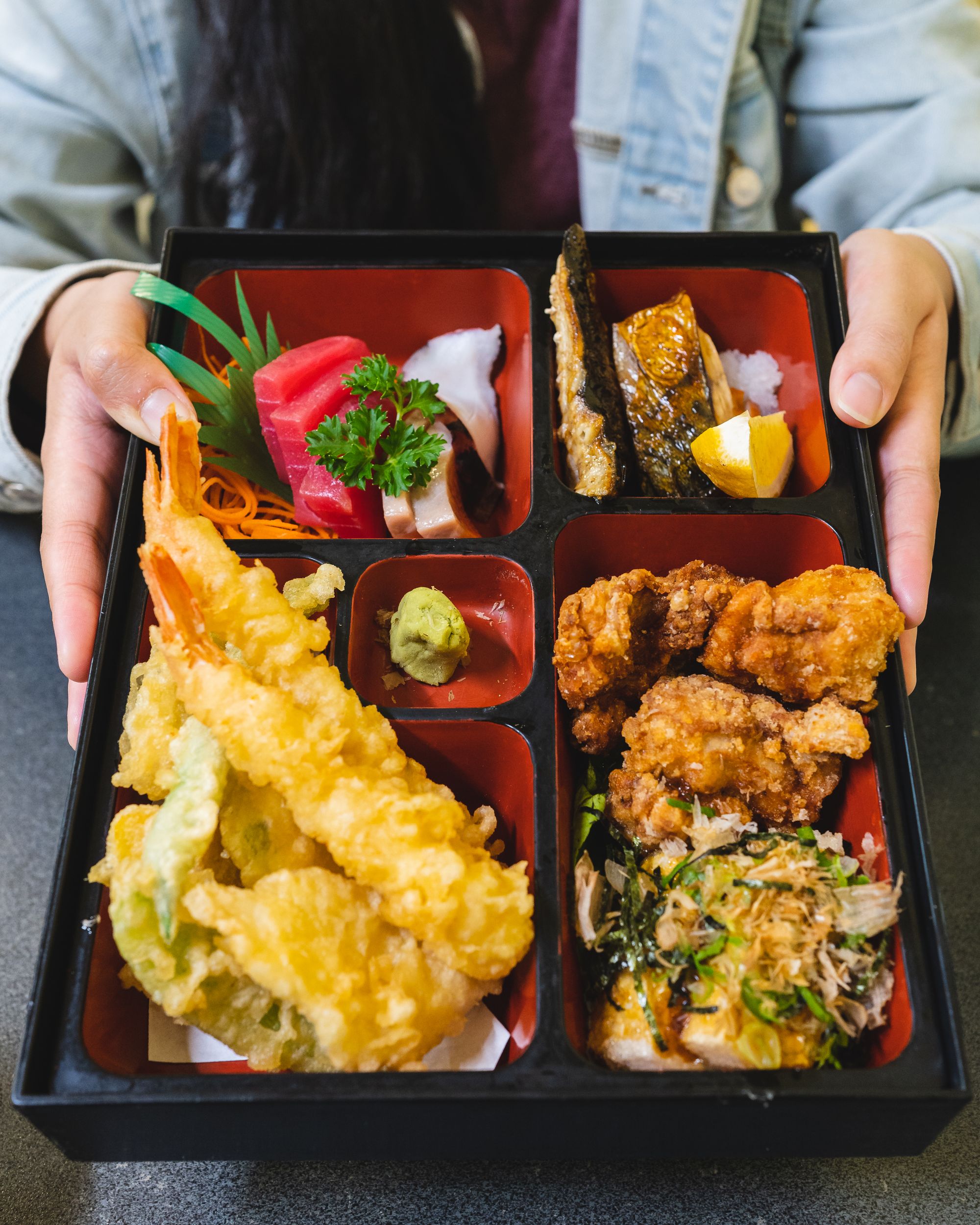 Hand holding a bento box full of Japanese dishes