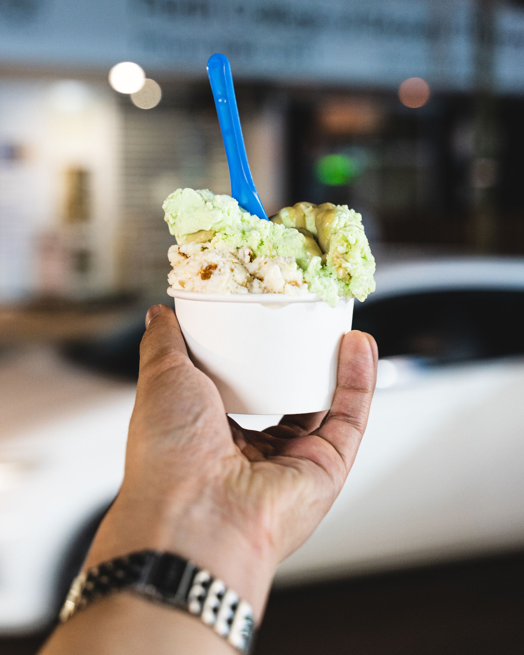 Hand holding cup of gelato with a blue spoon sticking out