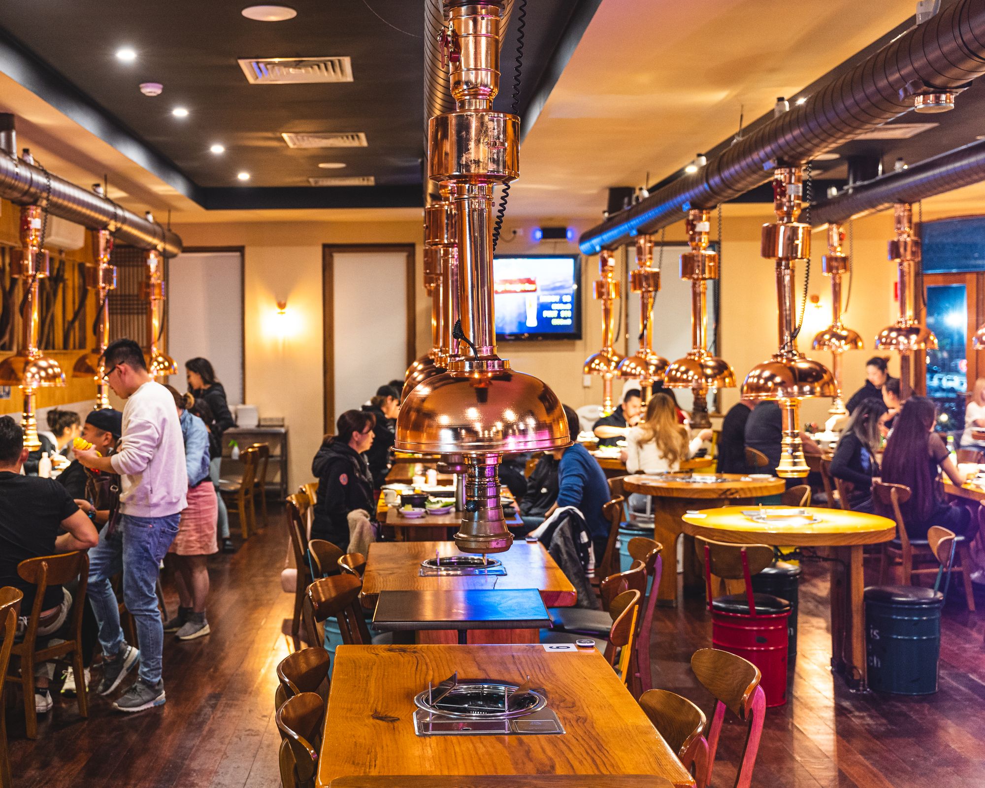 Interior shot of a bustling Korean BBQ restaurant showing BBQ tables and moveable exhaust pipes