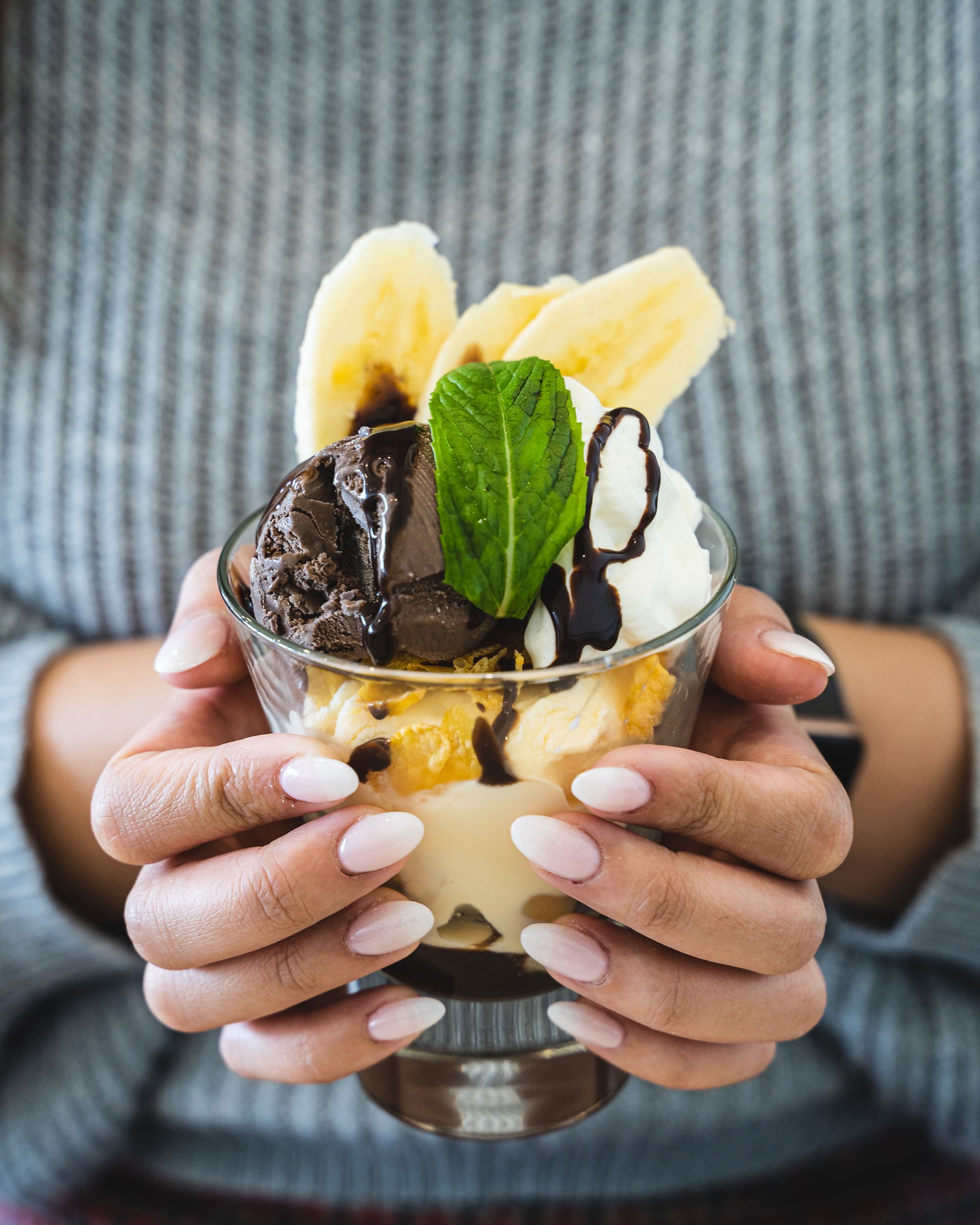 Pedicured hands holding a glace with a chocolate banana parfait inside