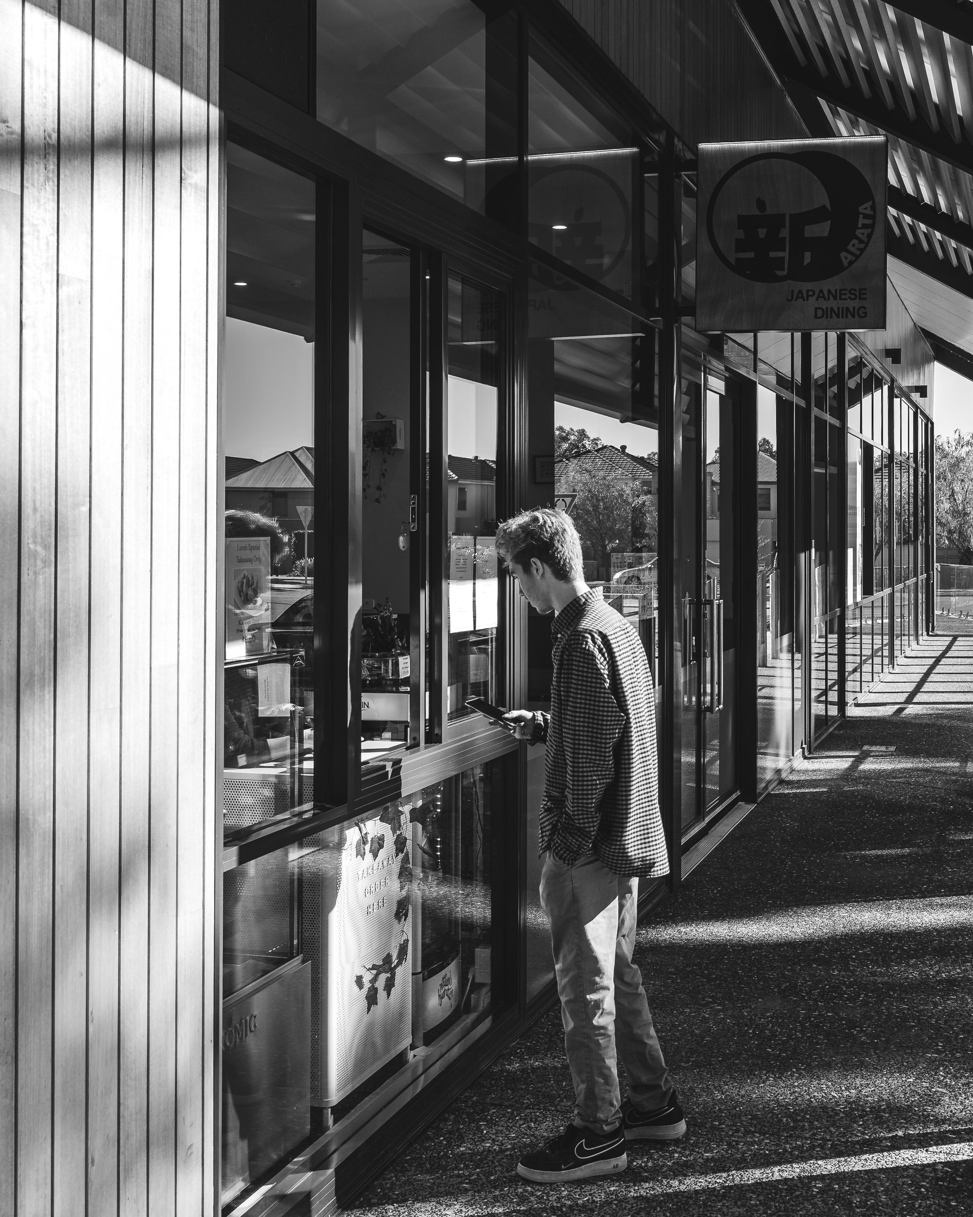 Black and white photo of a man ordering food outside of the takeaway window at Arata Dining