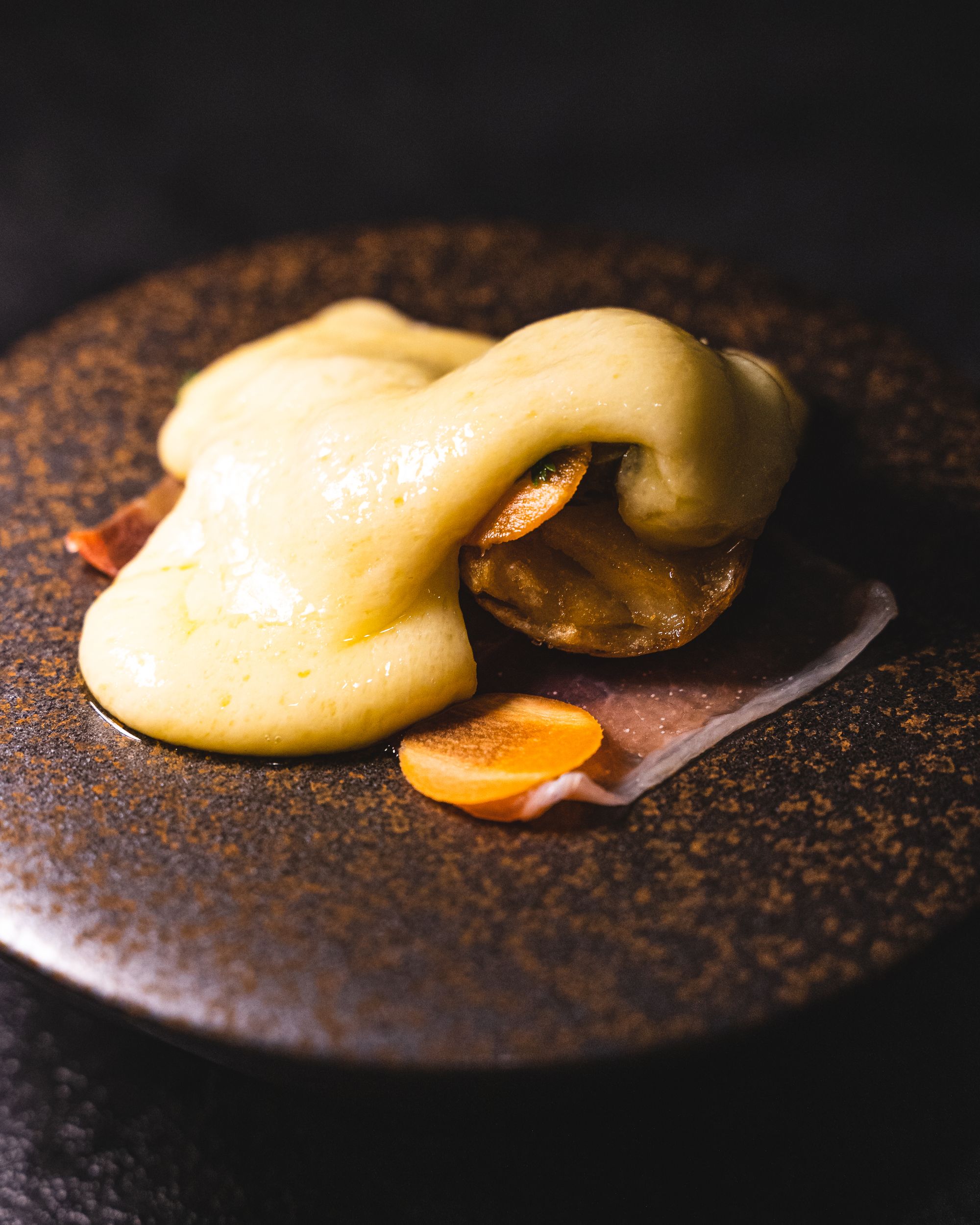 Close up of raclette on-top of jamon and a pickle