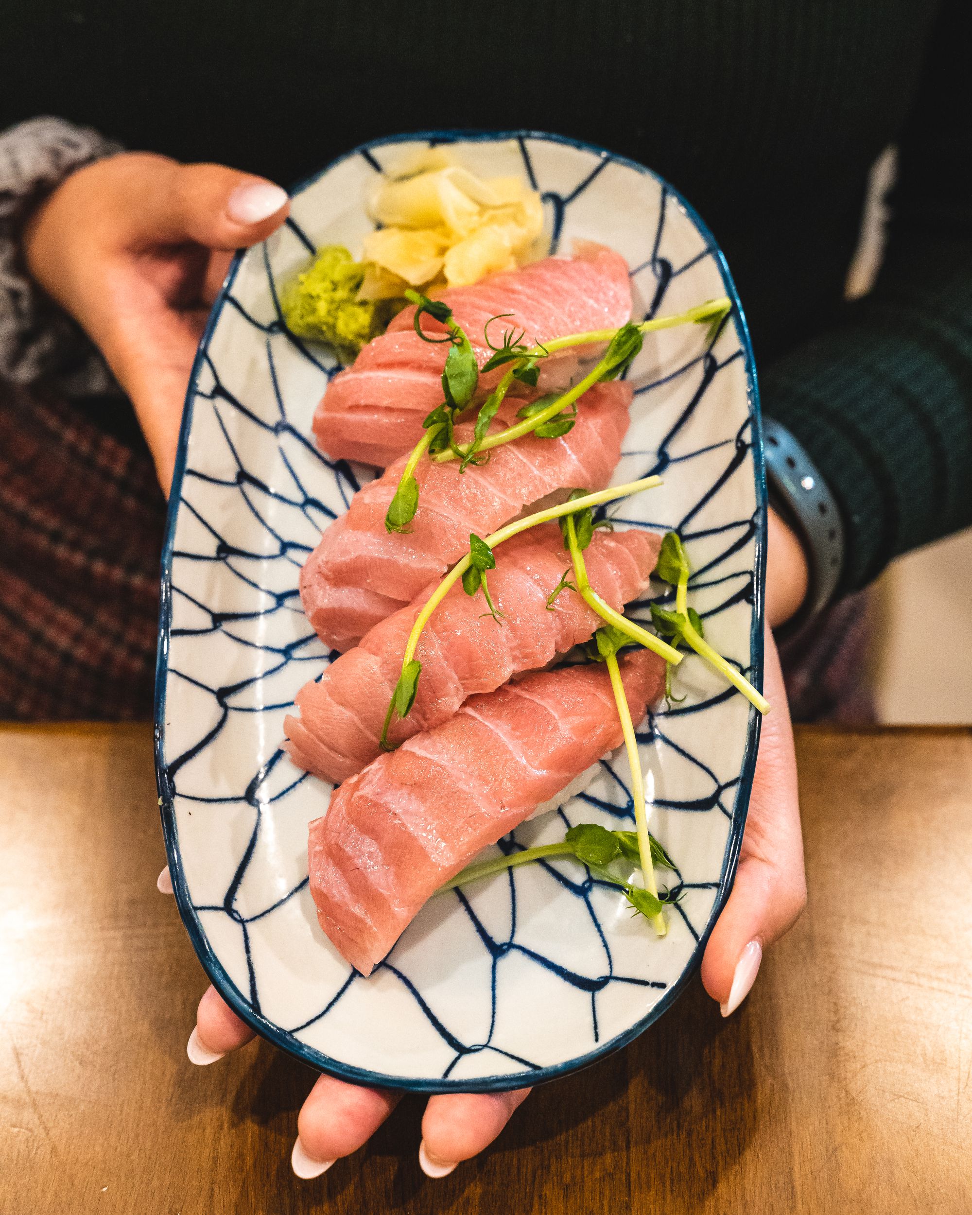 Manicured hands holding a plate of toro nigiri