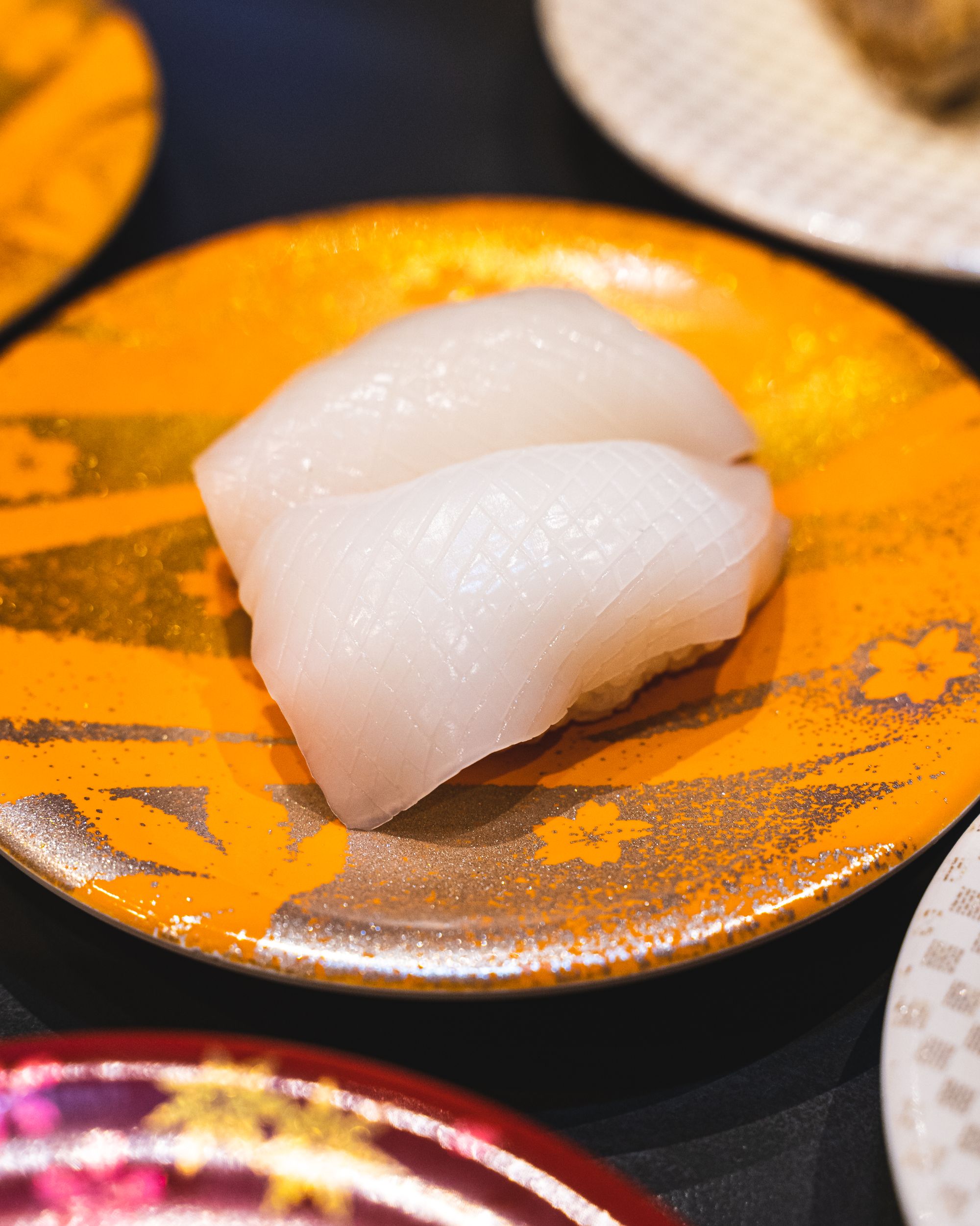 Close up of squid nigiri showing shallow knife cuts to absorb soy sauce