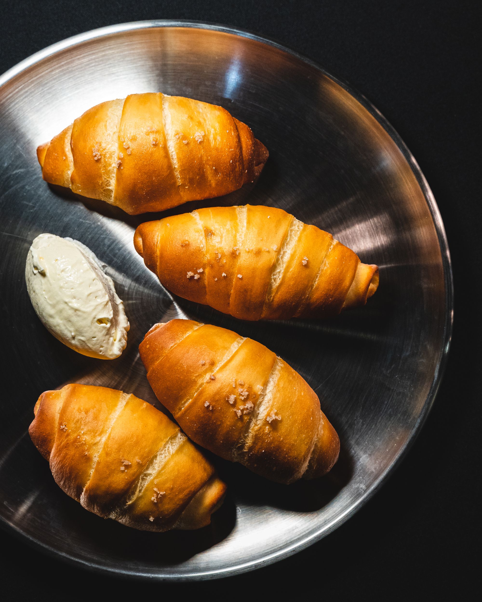 Top down shot of croissant shaped pastries on a metal plate with a quenelle of butter 