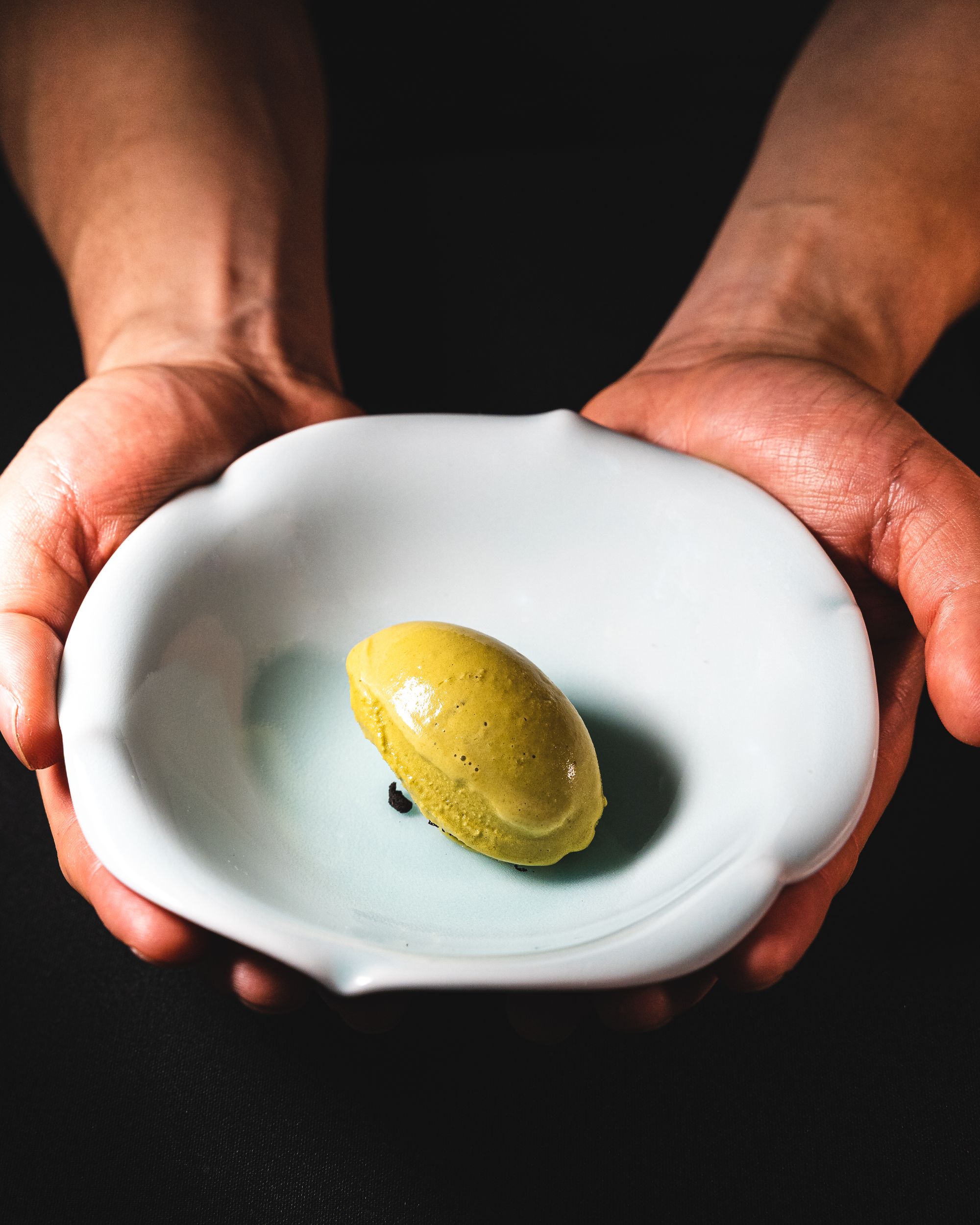 Hand holding a quenelle of mustard coloured ice-cream