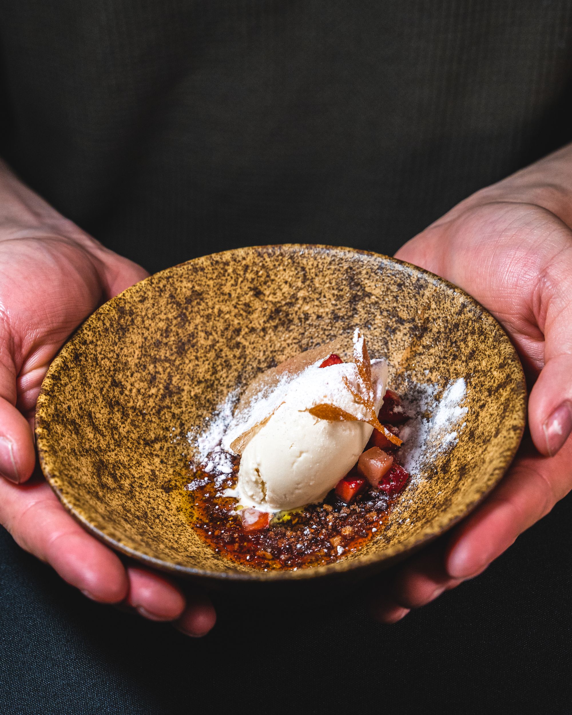 Hand holding a bowl with a quenelle of ice-cream and diced strawberry