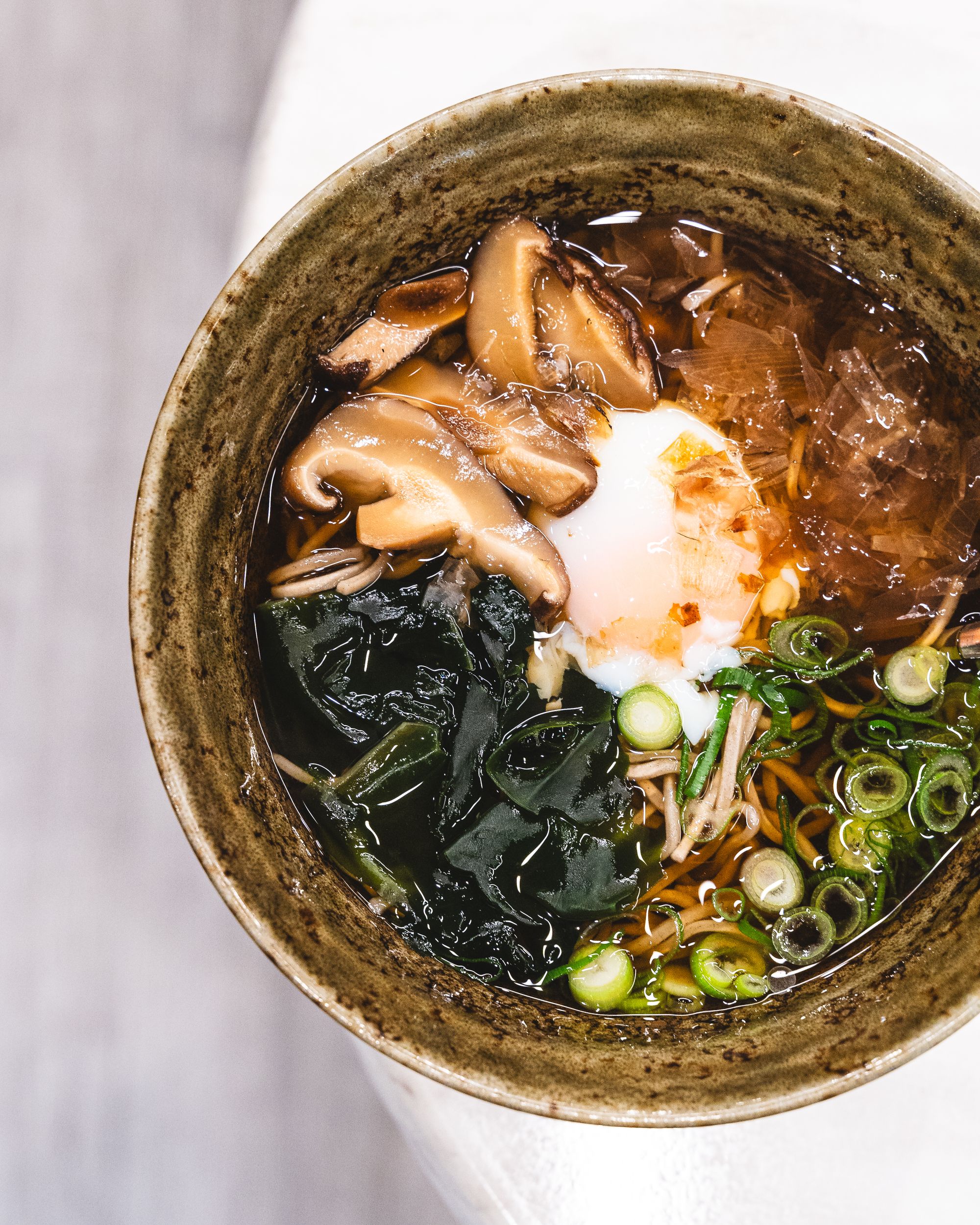 Top down shot of soba in bowl with spring onion, onsen egg and wakame