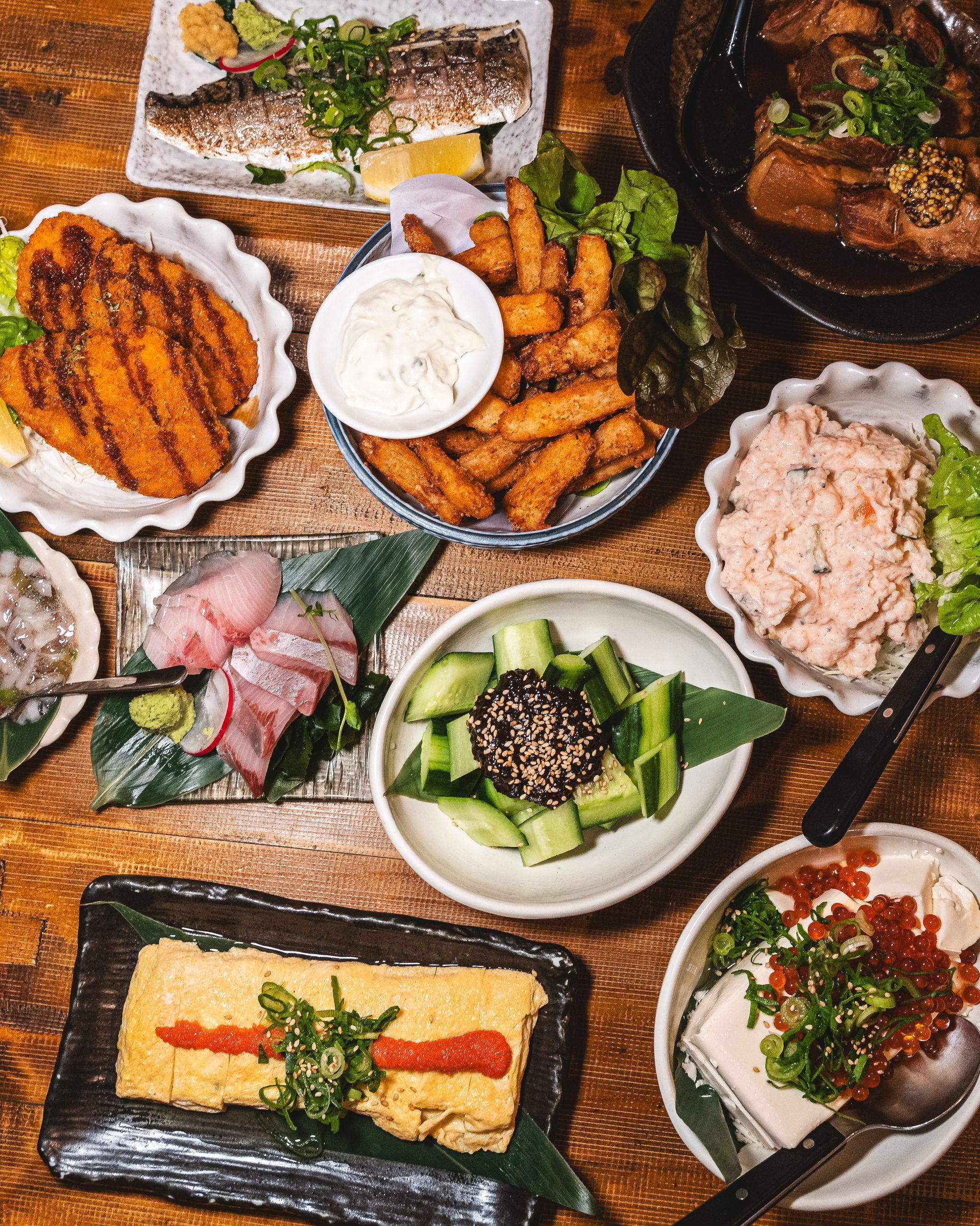 An assortment of Japanese izakaya dishes including miromi cucumber, tofu with ikura, potato salad, yam fries, croquette and grilled mackarel