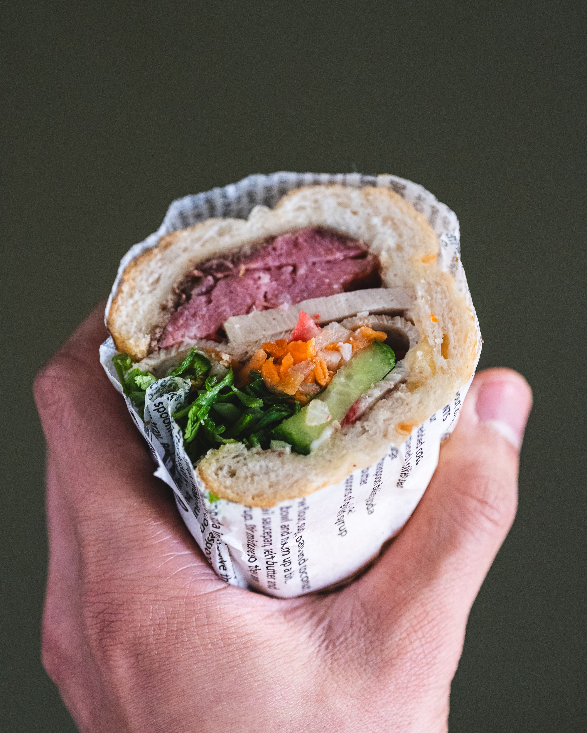 Close up of hand holding a cut banh mi with Vietnamese sausage, pickled carrot, coriander, cucumber and Vietnamese ham