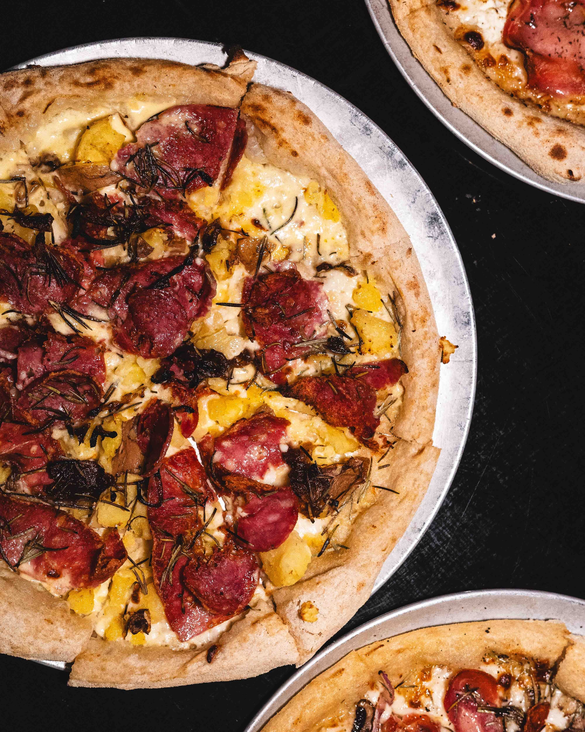 Top down photo of pizza with cacciatore, crushed potatoes and rosemary