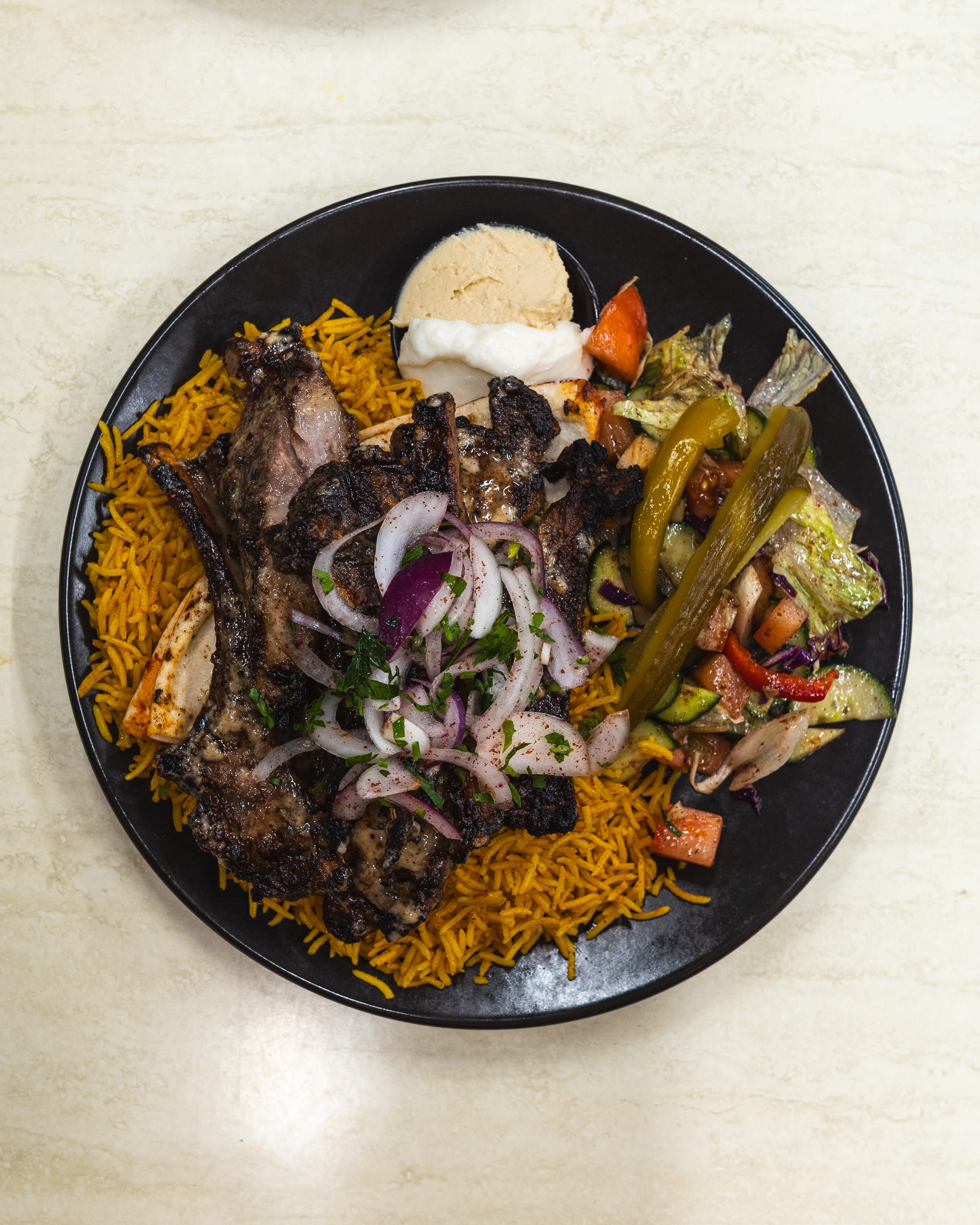 Top down shot of lamb cutlets on briyani rice with salad and hommus