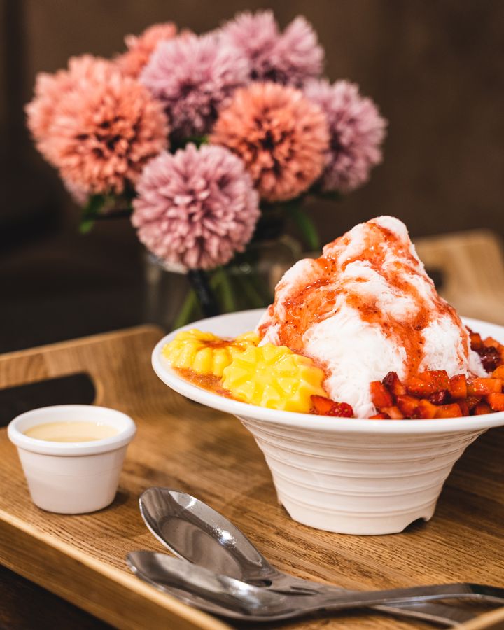 Shaved ice dessert with diced starwberry and egg pudding, in front of flowers
