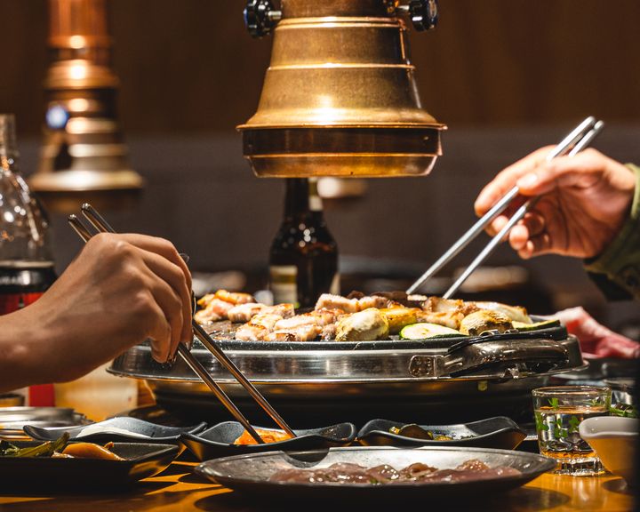 Two hands holding chopsticks enjoying Korean BBQ
